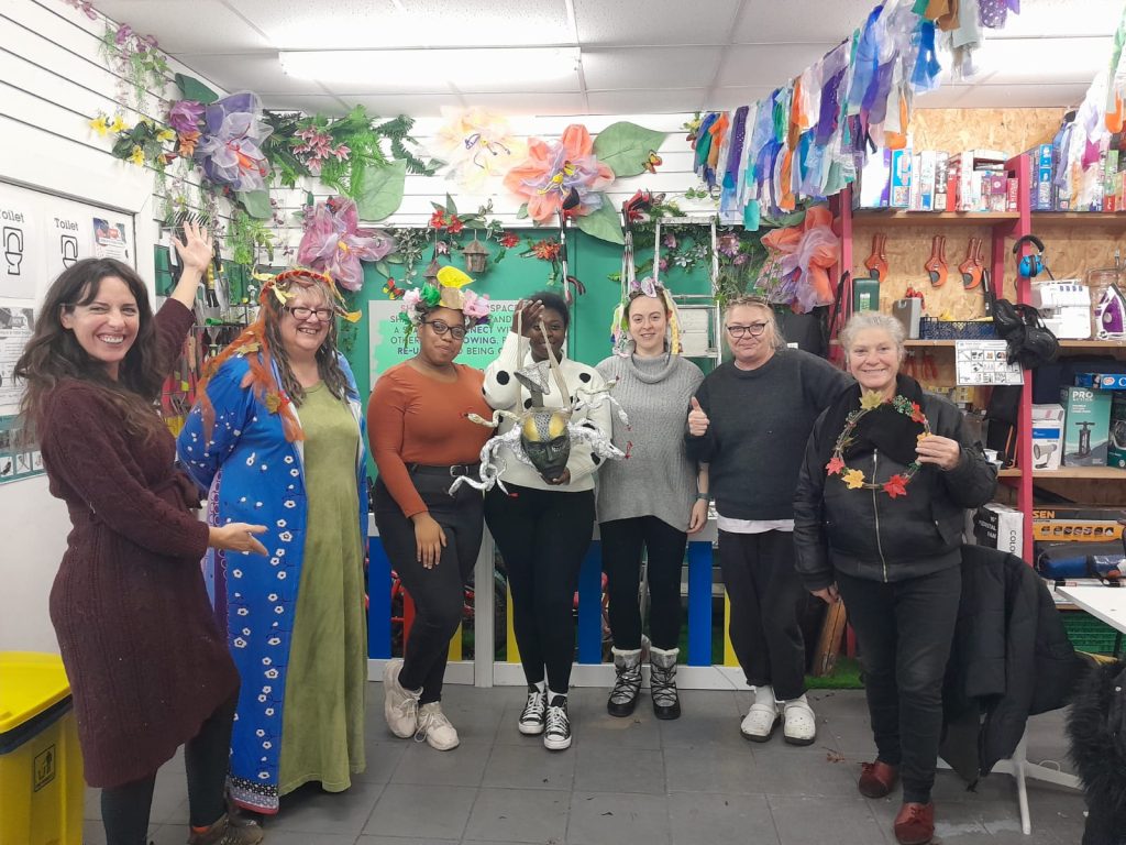 A group of women displaying the masks they have made at a workshop. They are in a colourful room at the Ladywood Share Shack.